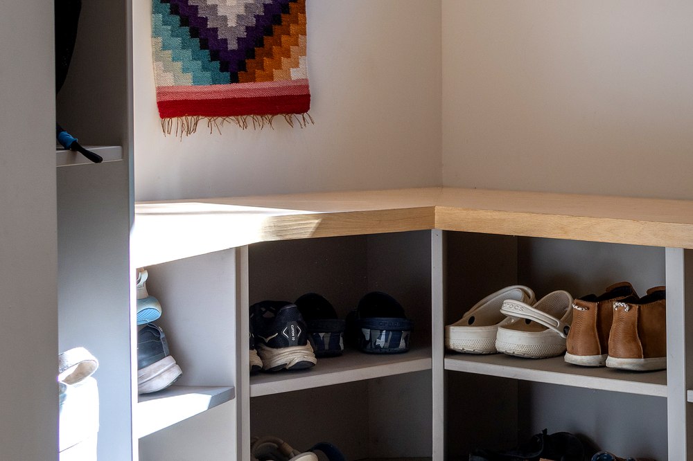 Storage bookshelf holding bags and hats above the bench